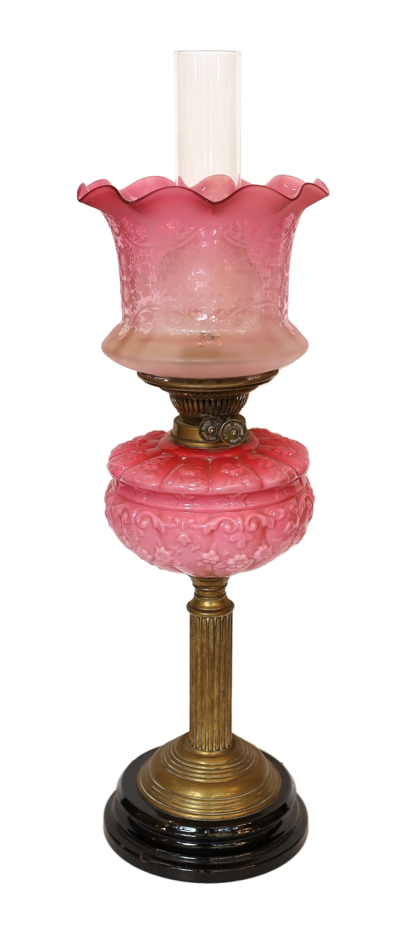 A late Victorian brass oil lamp with opaque pink glass reservoir, duplex mechanism, cranberry tinted etched glass shade and flue, height overall 65cm